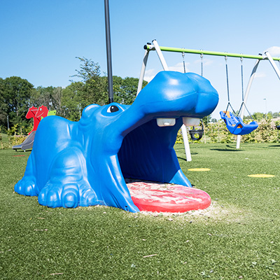 Ein Nilpferd in Form einer blauen Spielskulptur auf einem Spielplatz, mit geöffnetem Maul, das seine Zähne und seinen Mund zeigt.